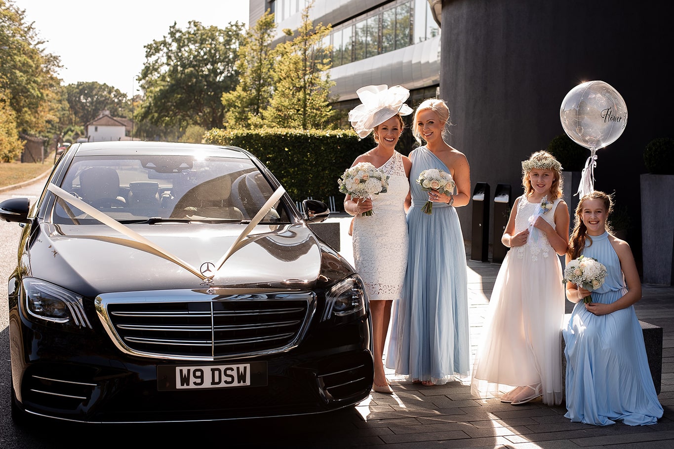 Bride and bridesmaids standing outside next to wedding balloon and black Mercedes wedding car